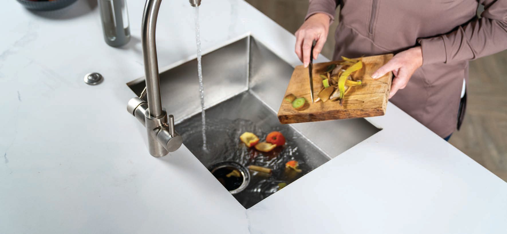 Persona echando restos de comida al fregadero con un triturador InSinkErator funcionando